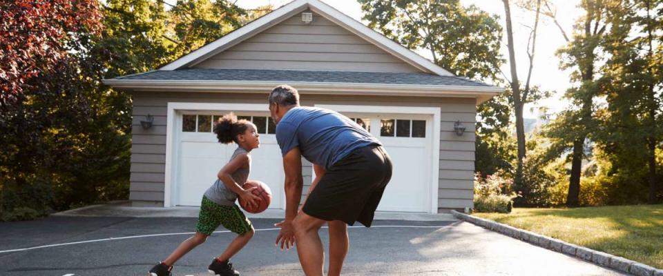 Father And Son Playing Basketball On Driveway At Home