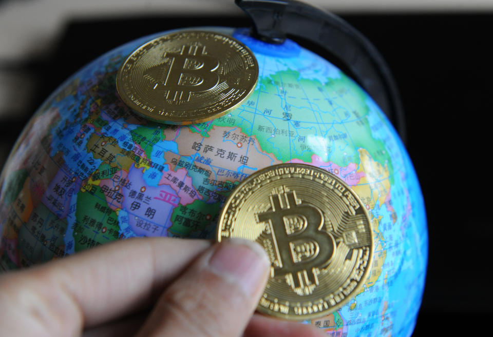 A Bitcoin being held against a representation of a globe. 