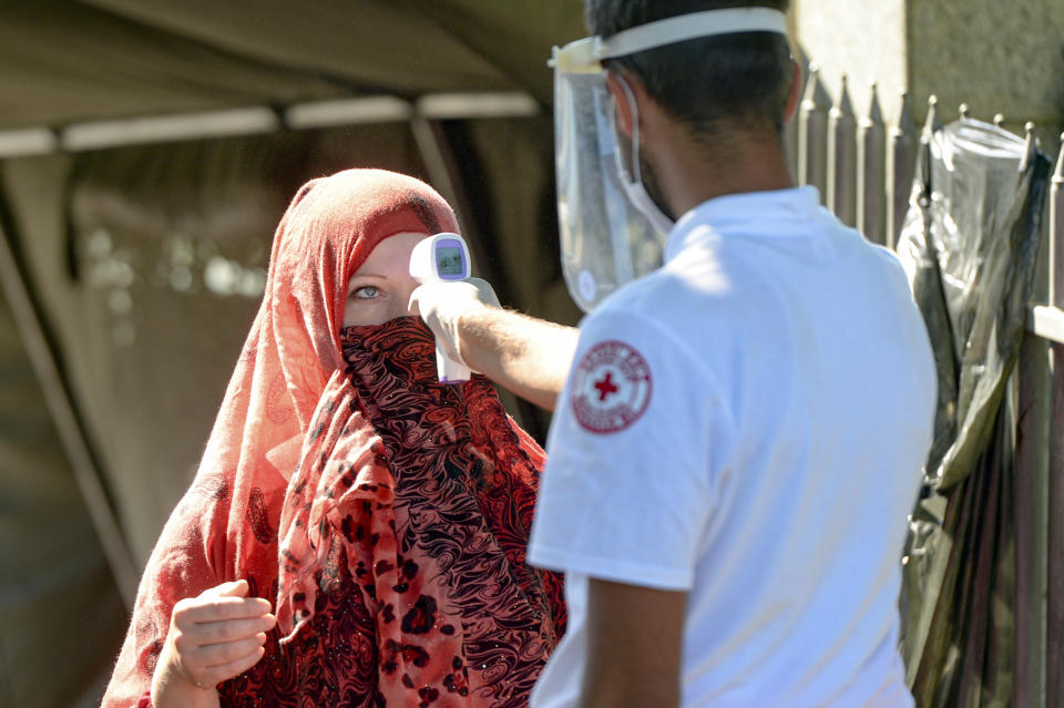 A health worker measures the temperature of a woman before granting her access to the memorial cemetery in Potocari, near Srebrenica, Bosnia, Saturday, July 11, 2020. Nine newly found and identified men and boys were laid to rest as Bosnians commemorate 25 years since more than 8,000 Bosnian Muslims perished in 10 days of slaughter, after Srebrenica was overrun by Bosnian Serb forces during the closing months of the country's 1992-95 fratricidal war, in Europe's worst post-WWII massacre. (AP Photo/Kemal Softic)