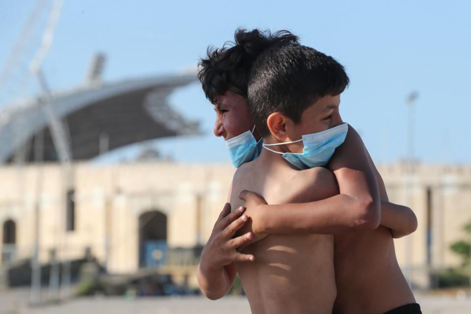 TOPSHOT - Mask-clad boys hug each other while playing football in front of the Camille Chamoun Sports City Stadium in the Lebanese capital Beirut amid the ongoing COVID-19 pandemic, on May 11, 2020. - Lebanon ordered a four-day-long lockdown to stem the spread of the coronavirus after recording an uptick in infections in recent days amid eased restrictions. (Photo by - / AFP) (Photo by -/AFP via Getty Images)