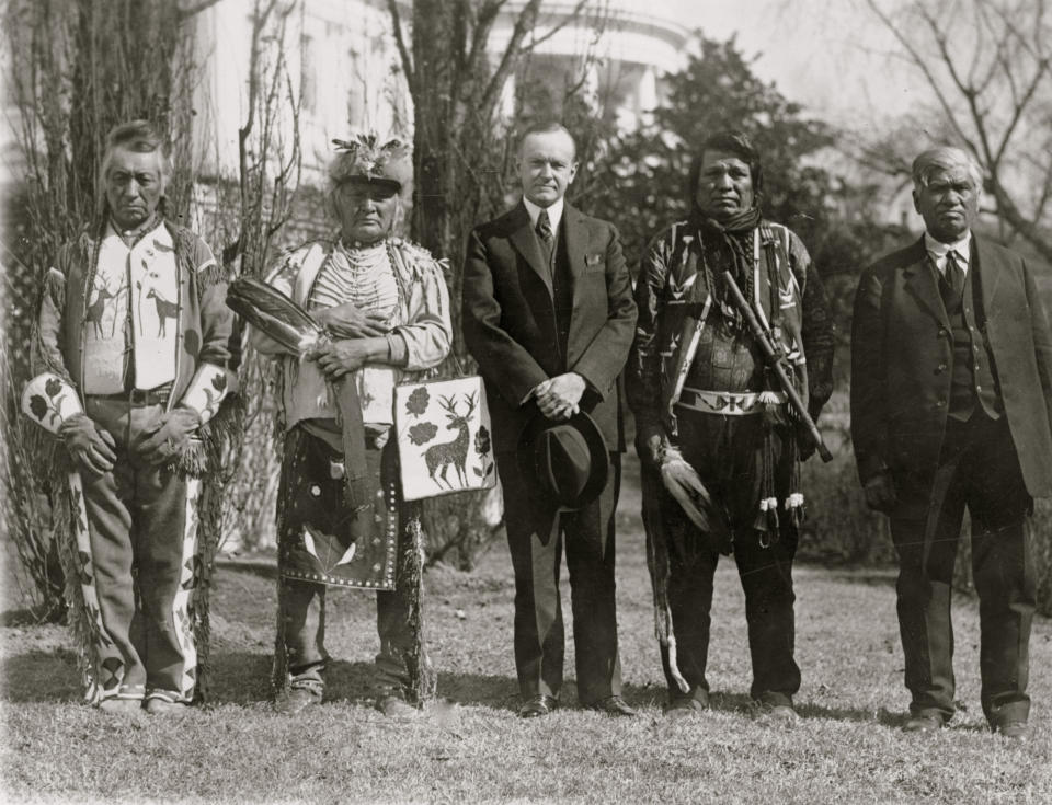 President Calvin Coolidge posed, full-length portrait, standing, facing front, with four Osage Indians, White House in the background, 1925. (Photo by National Photo/Buyenlarge/Getty Images)