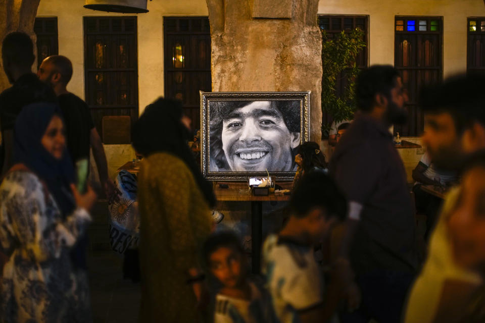 People walk past a painting of Argentinian soccer idol Diego Armando Maradona in a pedestrian area in downtown Doha, Qatar, Friday, Nov. 18, 2022. (AP Photo/Francisco Seco)