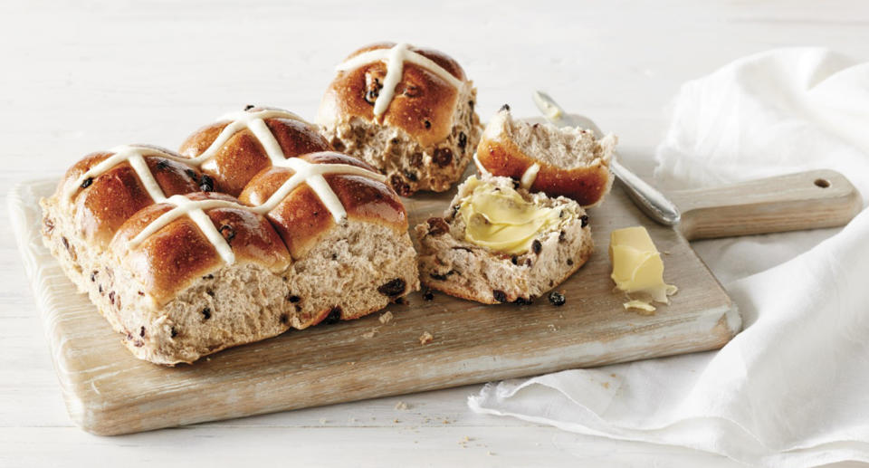 Hot cross buns served on a board with butter.