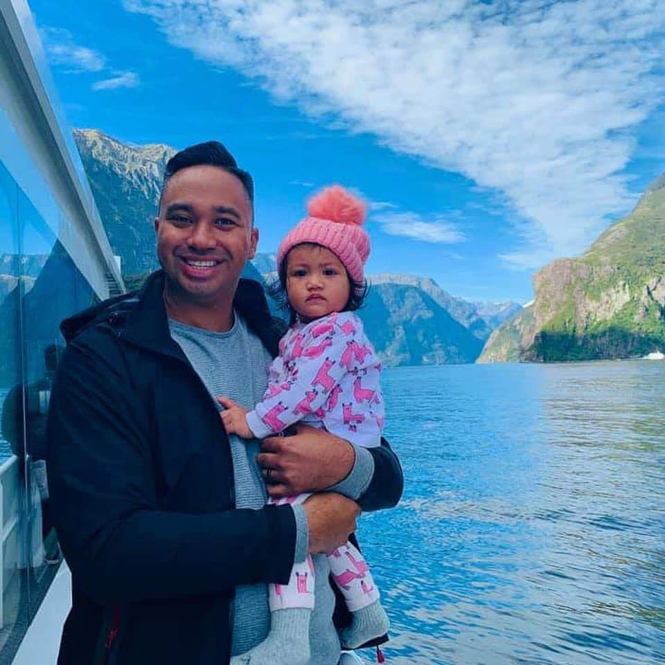 Harvee Pene holds his daughter Havana in front of a blue lake and mountains. 