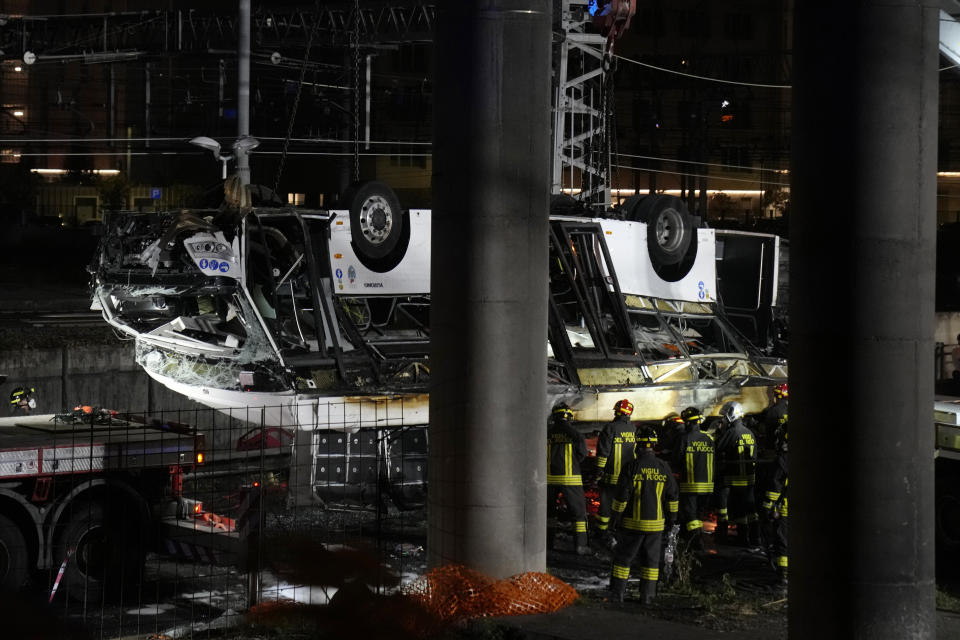 Italian firefighters work at the scene of a passenger bus accident in Mestre, near Venice, Italy, Wednesday, Oct. 4, 2023. According to local media, the bus fell a few meters from an elevated rod before crashing Tuesday close to Mestre's railway tracks, where it caught fire. (AP Photo/Antonio Calanni)