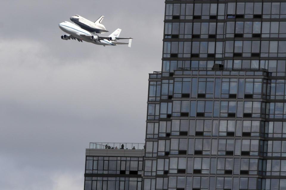People watch from the balcony of a building as the space shuttle Enterprise, riding on the back of the NASA 747 Shuttle Carrier Aircraft, cruises over the Hudson river, Friday, April 27, 2012 in New York. Enterprise is eventually going to make its new home in New York City at the Intrepid Sea, Air and Space Museum. (AP Photo/Mary Altaffer)