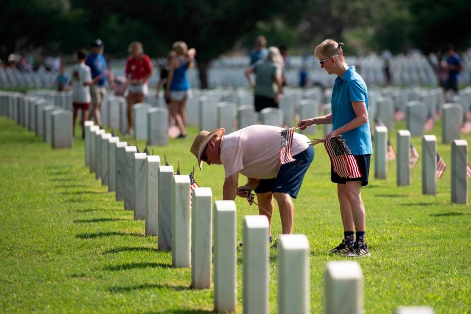 Volunteers help place thousands of tiny American flags on the graves of American service members at Biloxi National Cemetery in Biloxi ahead of Memorial Day on Saturday, May 25, 2024.