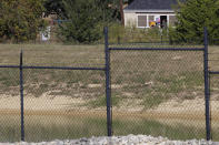 A staff member at the Mother's Heart Learning Center, in background, opens a door to let children inside from the center's playground in Arlington, Texas, on Monday, Oct. 25, 2021. The fracking pond in the foreground is part of a natural gas drill site, known as "AC-360," a few hundred feet from the daycare. The site is operated by TEP Barnett, a subsidiary of French energy giant Total Energies. It is one of Total's 33 well sites in Arlington containing 163 natural gas wells, most of them tucked in urban neighborhoods in Arlington. (AP Photo/Martha Irvine)