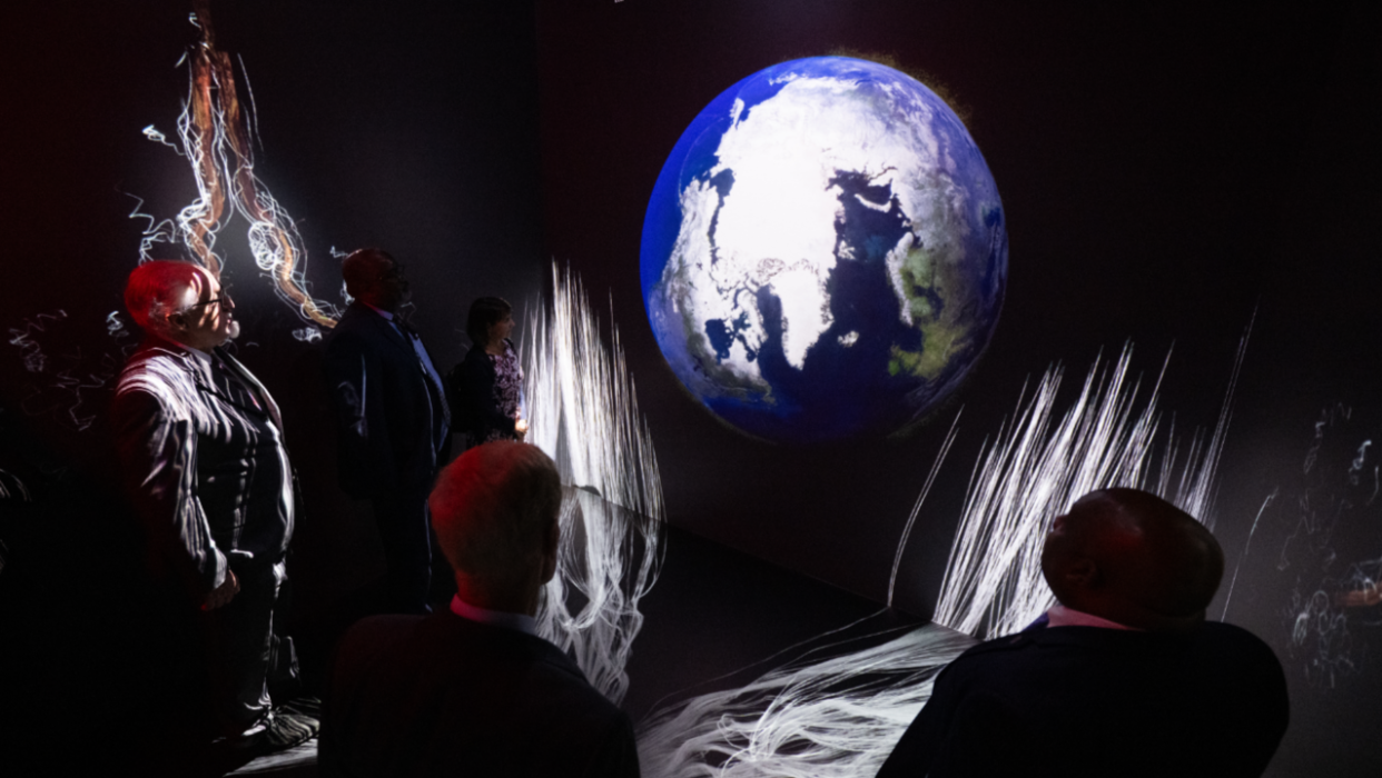  NASA experts stand in a dark room with Earth visualizations to show the impacts of climate change. 