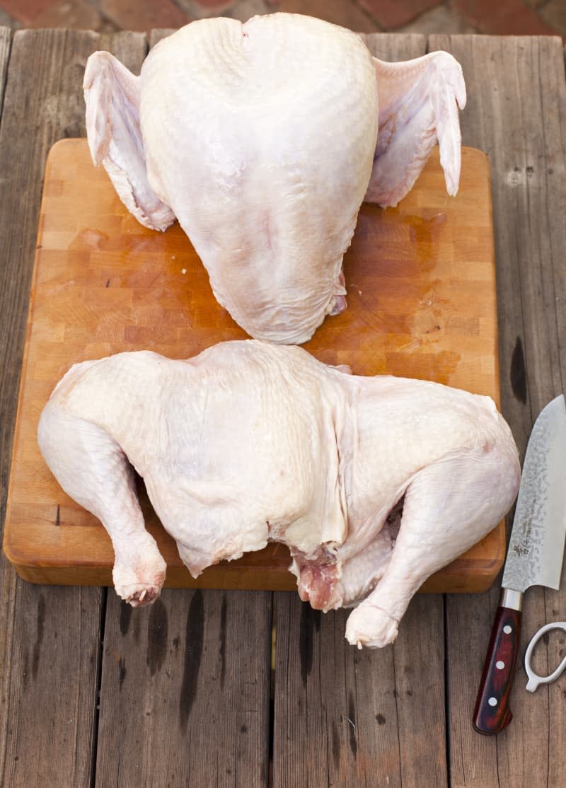 A whole turkey and a spatchcocked turkey on a wooden chopping board, with a knife on the side