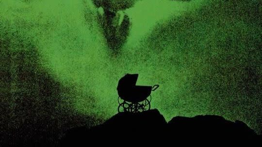 a baby carriage sits on top of an ominous craggy surface with a green glow and the face of roesmary behind it in the poster for rosemary's baby a good housekeeping pick for best halloween movies