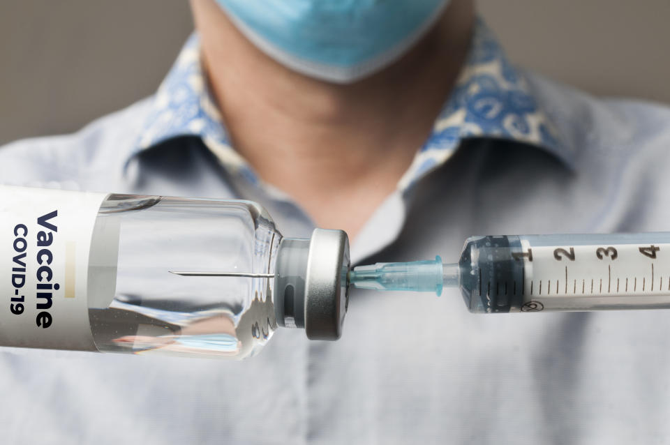 Doctor with surgical mask fills a syringe with the covid-19 vaccine to inject it