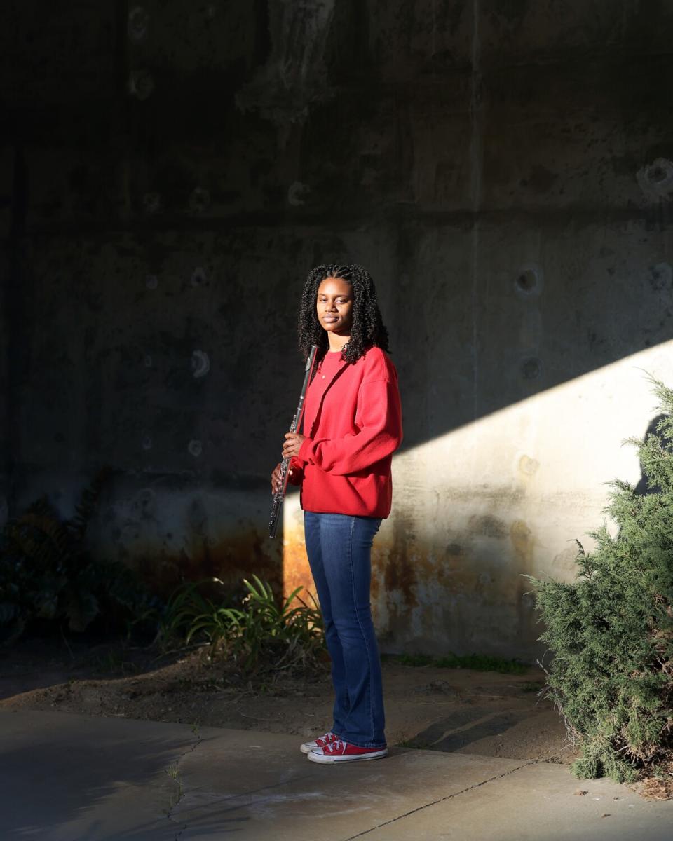 A young woman stands with her flute for a portrait.