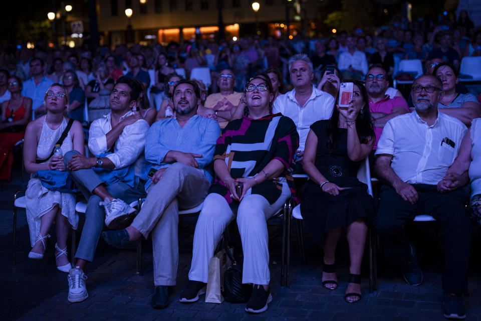 Spain's tenor Jorge de Leon, third left, Italian soprano Anna Pirozzi, third right, and opera singer German Olvera, second left, watch a broadcast of their show, Giacomo Puccini's Turandot in a square outside Teatro Real opera house in Madrid, Spain, Friday, July 14, 2023. For the past eight years, Madrid’s Teatro Real opera house has held a week of opera broadcasting shows that have been staged in the theater to towns and cities around Spain for free. The aim is to try to spread interest in the art form among the public and rid it off its elitist tag. This July, the highlight was Giacomo Puccini’s masterpiece, Turandot. (AP Photo/Bernat Armangue)
