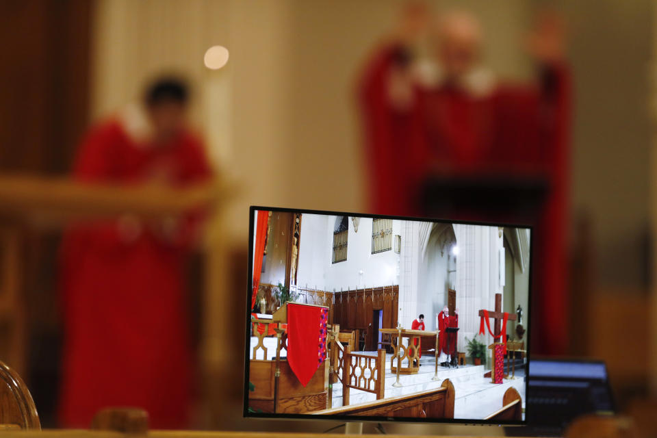 A video monitor displays what a camera is viewing as Deacon Antonio Guerrero, back left, and Father Jim Spahn, O.P., deliver by internet a broadcast of the Good Friday Mass at St. Dominic Catholic Church Friday, April 10, 2020, in Denver. The new coronavirus causes mild or moderate symptoms for most people, but for some, especially older adults and people with existing health problems, it can cause more severe illness or death. (AP Photo/David Zalubowski)