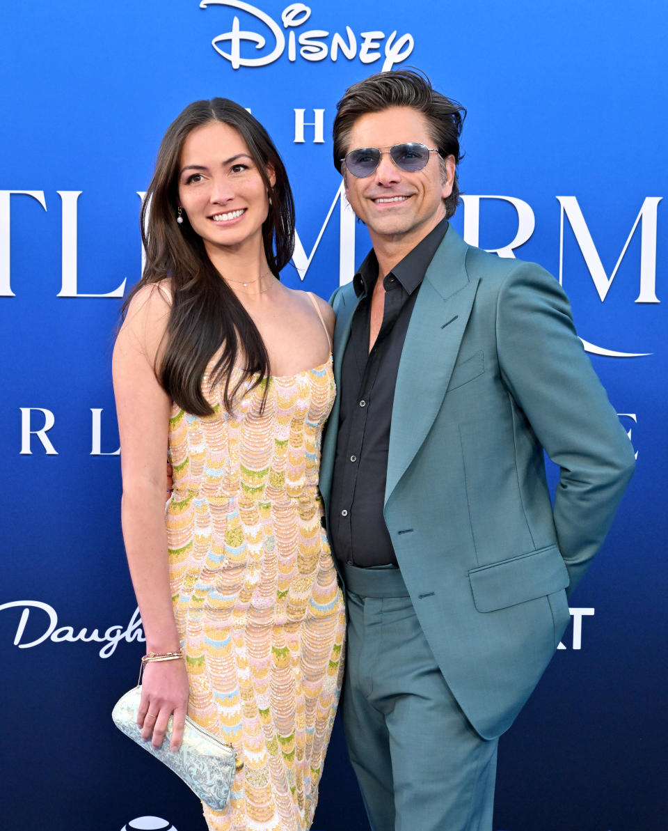 Two people posing together; one in a patterned dress and the other in a teal suit on a branded backdrop