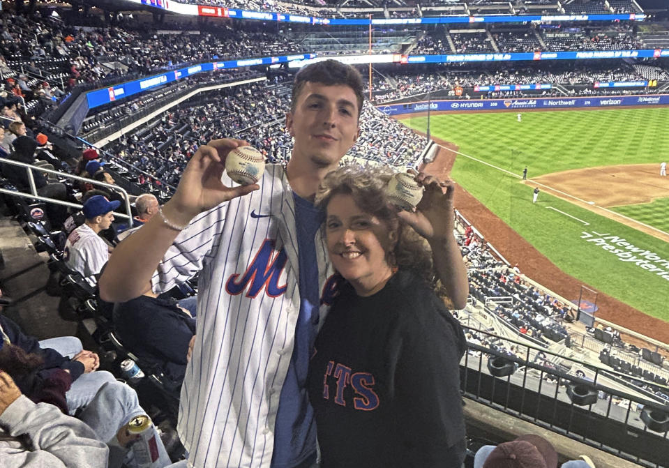 In a photo provided by Jerry Beach, Patrick Wedderburn, standing with his mother, Christa, holds two foul balls that he caught in a three-pitch span at the baseball game between the Cincinnati Reds and the New York Mets on Friday, Sept. 15, 2023, in New York. “I’m gonna give her both of them,” he said as he gestured to his mother, who was at the park as part of her birthday celebration. (Jerry Beach via AP)