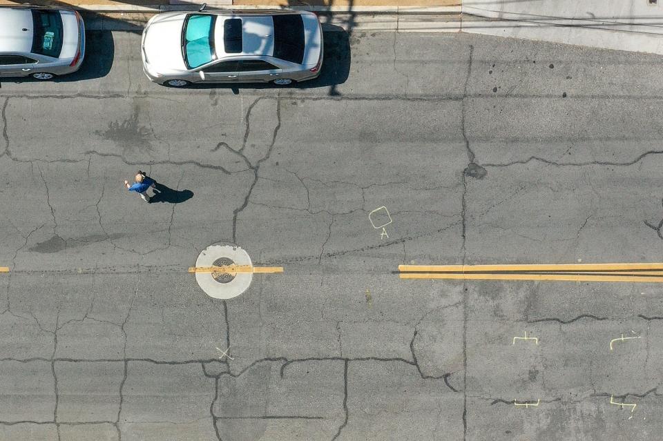 A pedestrian crosses Alessandro Drive in Palm Desert near the yellow police evidence markings from where Mike Satcher was killed by a car while crossing the street in May 2023.