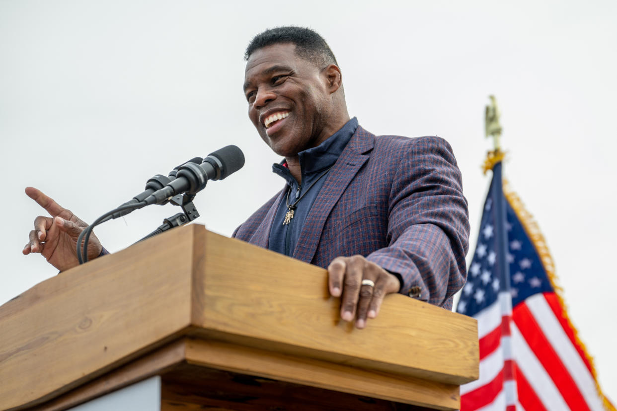Herschel Walker, looking upbeat, at the microphone, with a U.S. speaks to supporters with a U.S. flag flying  behind him