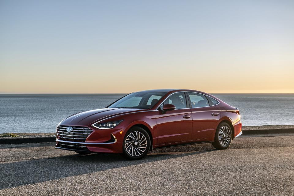 A Hyundai Sonata Hybrid sits parked on a beach overlooking water and a sunrise.