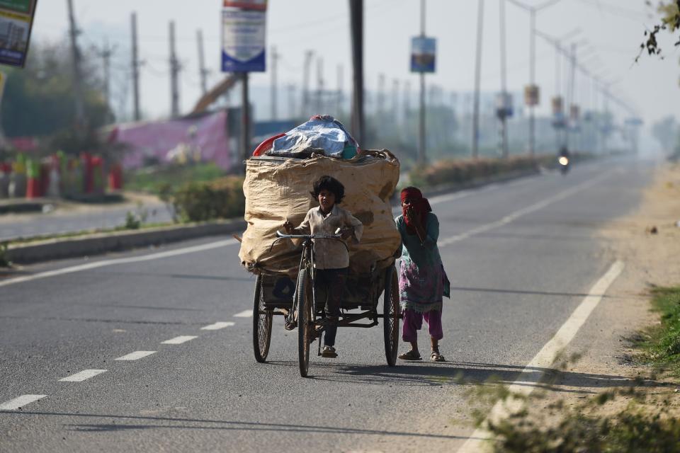 A child pulls a garbage cycle rickshaw as his mother pushes it along a street during Covid-19 curfew in Haryana on 22 March, 2020. (AFP via Getty Images)