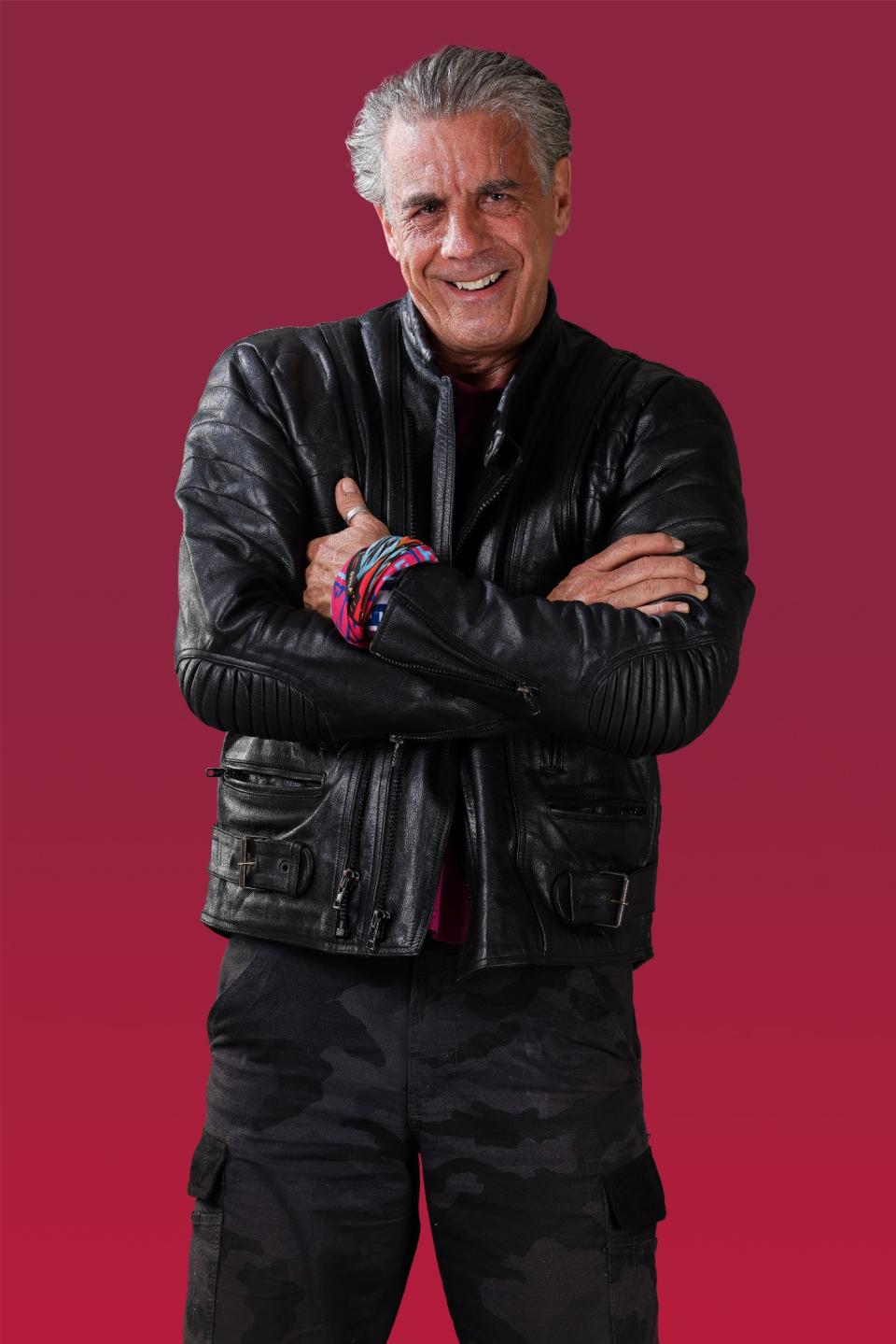 Garrick wears a black leather jacket and black pants and smiles at the camera.