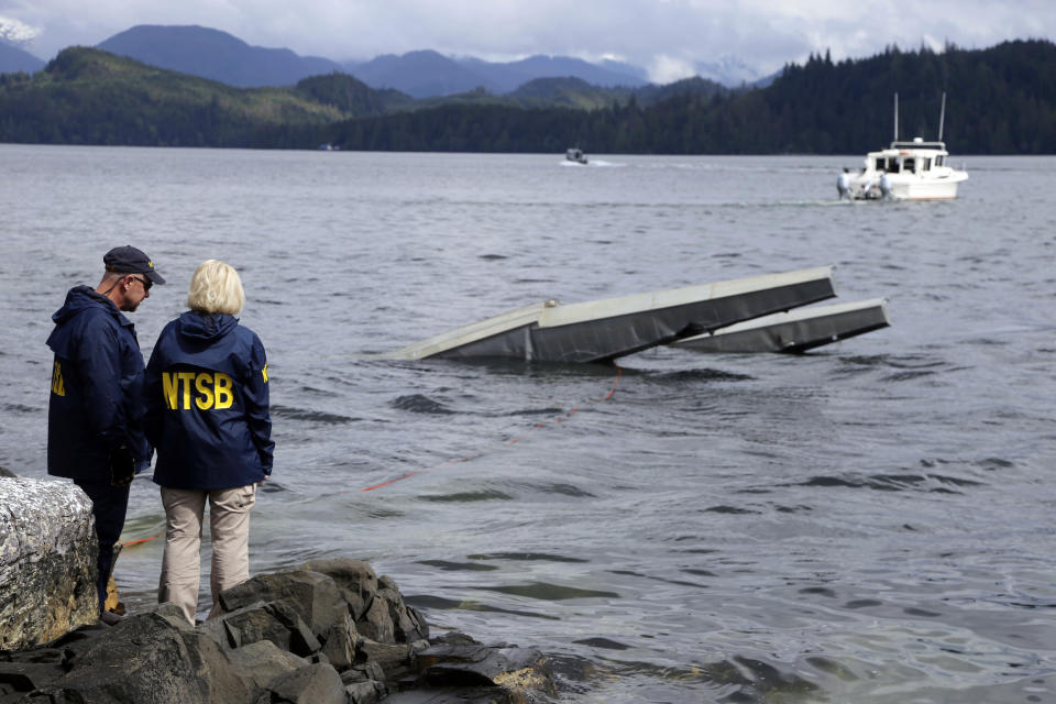 FILE - In this May 15, 2019 file photo provided by the National Transportation Safety Board, NTSB investigator Clint Crookshanks, left, and member Jennifer Homendy stand near the site of some of the wreckage of the DHC-2 Beaver that was involved in a midair collision near Ketchikan, Alaska, a couple of days earlier. A preliminary report released Wednesday, May 22, 2019 says a pilot saw a flash on his left side just before his plane collided with another plane in Alaska, killing six people. The National Transportation Safety Board says in the report released Wednesday, May 22, 2019, that the two planes carrying Alaska cruise ship passengers were returning from a flightseeing tour of Misty Fjords when the collision occurred May 13 northeast of Ketchikan. (Peter Knudson/NTSB via AP, File)