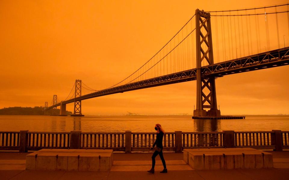 A woman walks under an orange smoke-filled sky in San Francisco - Getty