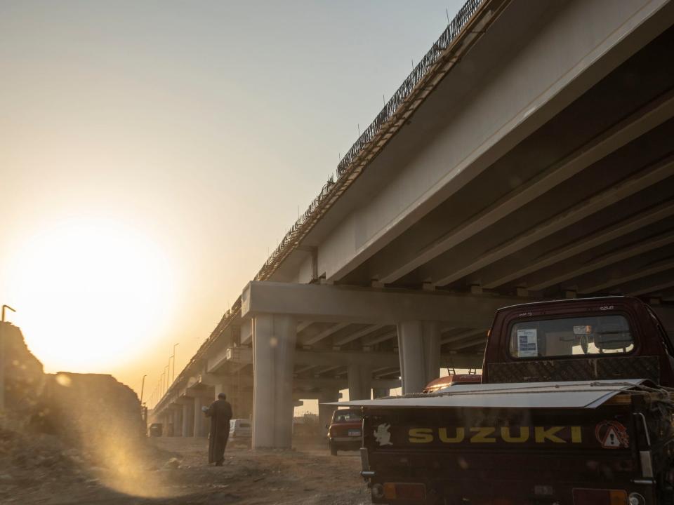 A man walks under a new highway under construction through the City of the Dead.