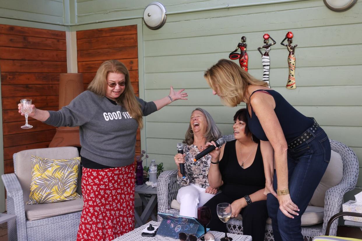 Four women sing karaoke and drink out of wine glasses