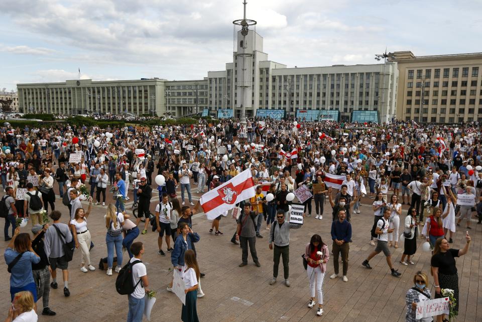 People, many holding old Belarusian national flags as they gather at Independent Square in the center of Minsk, Belarus, Friday, Aug. 14, 2020. Some thousands of people flooded the centre of the Belarus capital, Minsk, in a show of anger over a brutal police crackdown this week on peaceful protesters that followed a disputed election. (AP Photo/Sergei Grits)