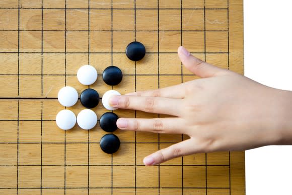 A hand placing a white Go piece on a Go board