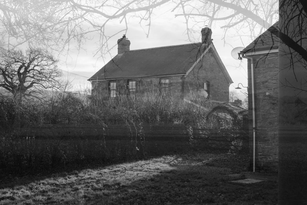  A black and white double exposure of a farmhouse with the silhouette of trees around the edges of the frame. 