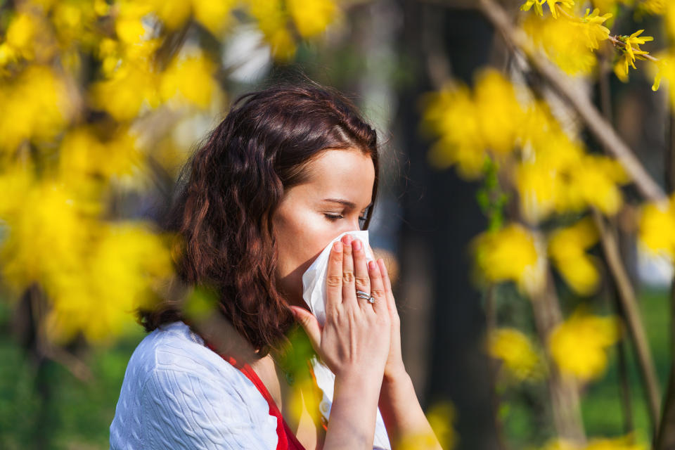 Portrait of a young brunette woman blowing her nose when standing close to flowers in a park