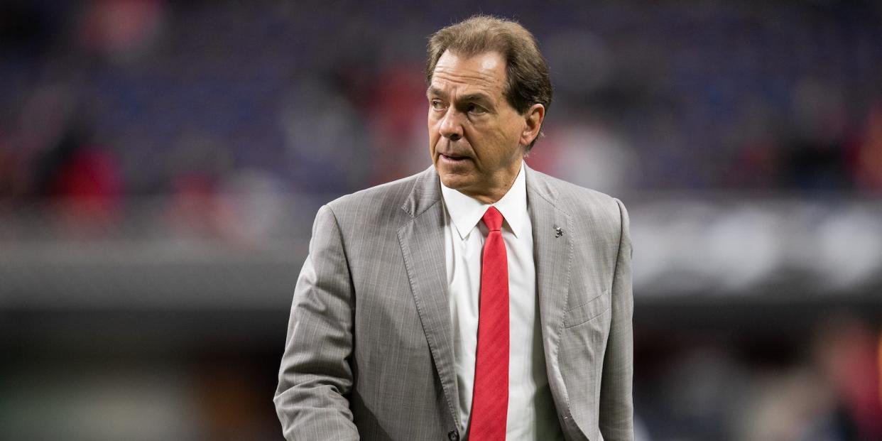 Nick Saban walks onto the field wearing a suit and tie.