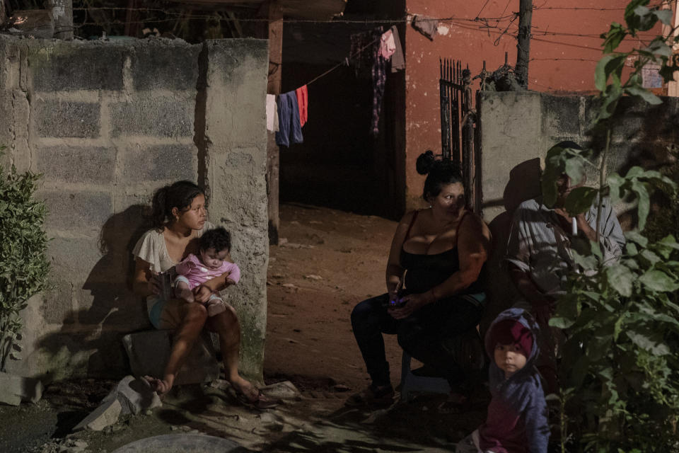 A family sits outside their home as forensic workers investigate a body at a crime scene in the Rivera Hernandez neighborhood of San Pedro Sula, Honduras on Nov. 30, 2019. MS-13. Mara 18. Los Vatos Locos _ The Crazy Guys. The gangs' shifting lines of control dodge and weave through Rivera Hernandez, a place where even the police are afraid. (AP Photo/Moises Castillo)