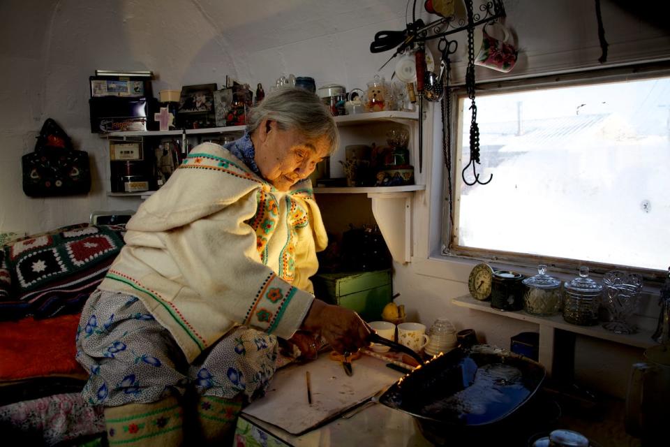 Qapik Attagutsiak of Arctic Bay, Nunavut, lights a qulliq — a traditional oil lamp — in her home.