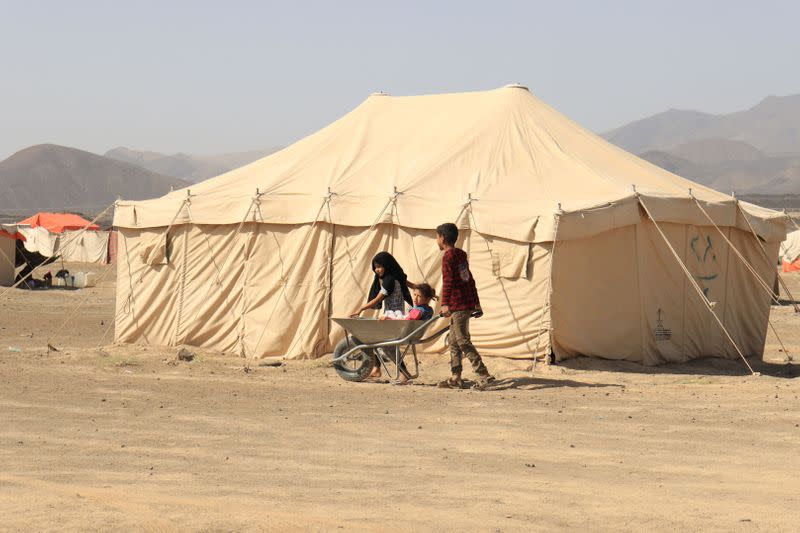 Boy pushes a wheelbarrow with girls on it at a camp for internally displaced people (IDPs) in Marib