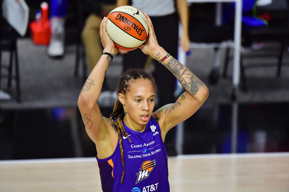 Brittney Griner in a purple Mercury jersey holds a basketball above her head. 