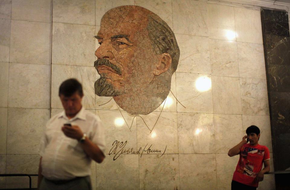 Men use their mobile phones as they stand in front of a mosaic depicting former Soviet leader Vladimir Lenin at Biblioteka Imeni Lenina metro station in Moscow August 13, 2013. To step onto the Moscow metro is to step back in time and immerse yourself in a museum rich in architecture and history. Opened in 1935, it is an extravagant gallery of Communist design, featuring Soviet artworks, statues, chandeliers, stained glass and ceiling mosaics. Built under Stalin, the metro now transports 7 to 9 million people a day and costs 30 Rubles, around $1, for a single ride. Picture taken August 13, 2013. REUTERS/Lucy Nicholson (RUSSIA - Tags: SOCIETY TRANSPORT TPX IMAGES OF THE DAY) ATTENTION EDITORS: PICTURE 11 OF 24 FOR PACKAGE 'RIDING THE MOSCOW METRO' SEARCH 'MOSCOW CHANDELIERS' FOR ALL IMAGES