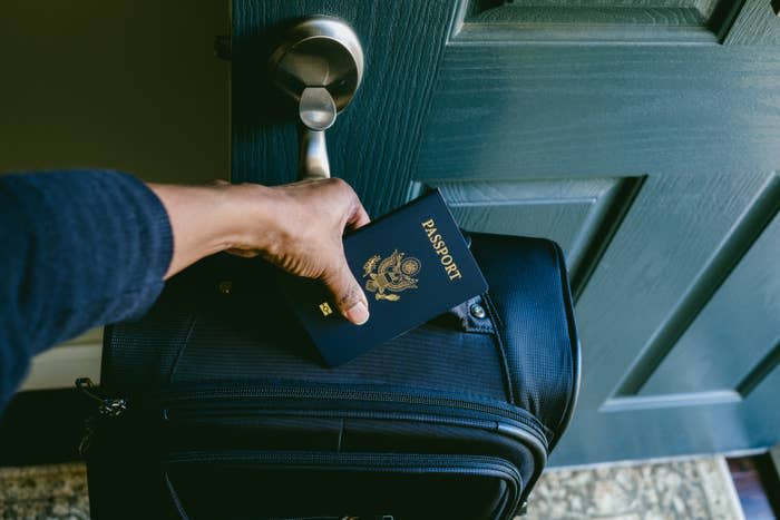 Person holding a passport while touching a suitcase handle, indicating travel preparation