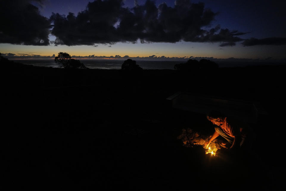 Pascal Boulineau, the husband of French-born artist Delphine Poulain, tends to a campfire outside their home in Hanga Roa, Rapa Nui or Easter Island, Wednesday, Nov, 23, 2022. On one of her trips back to France, Poulain fell back in love with the man who had been her teenage boyfriend. Now they have two children of their own, and the four of them have made a home in Rapa Nui since 2014.( AP Photo/Esteban Felix)