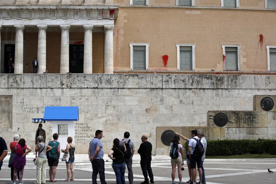 Tourists look the red paint on the wall of the Parliament building in Athens, Tuesday, May 21, 2019. A group of about 10 people threw red paint at parliament and set off a smoke bomb as Greece's Supreme Court heard an appeal against the denial of a temporary leave of absence from prison of a hunger striking extremist serving multiple life sentences for the killings of 11 people by the country's deadliest far-left group. (AP Photo/Thanassis Stavrakis)