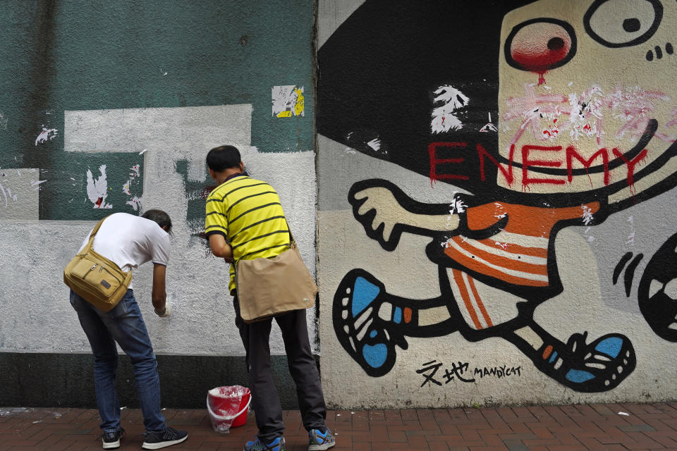 eIn this Sept. 16, 2019, photo, two workers clean up after painters are painting the wall in Hong Kong after protesters had scribbled multiple anti-government graffiti on it. The eye on the mural is painted red. An eye patch became a symbol of the fight for freedom after a young woman sustained a severe eye injury during an anti-government protest. (AP Photo/ Vincent Yu)