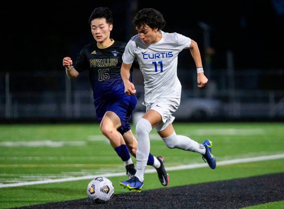 Curtis midfielder Julian Valencia (11) races down the sideline with the ball as Puyallup defender Jet Hazen (15) tries to steal the ball from him during the second half of a 4A Pierce County League boys varsity soccer game at Sparks Stadium in Puyallup, Wash. on May 1, 2023. The teams tied the game 2-2.