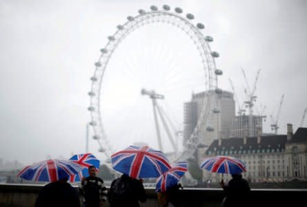FILE PHOTO: Tourists carrying Union Flag umbrellas shelter from the rain in front of the London Eye wheel in London, Britain, August 9, 2017. REUTERS/Hannah McKay/File Photo