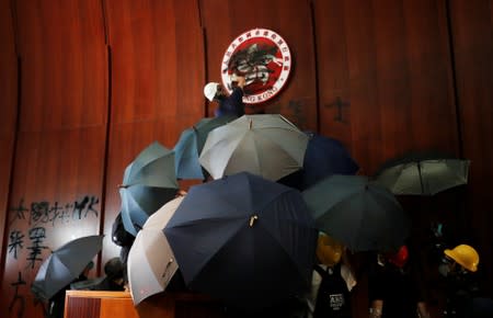 A person sprays paint over Hong Kong's coats of arms inside a chamber after protesters broke into the Legislative Council building during the anniversary of Hong Kong's handover to China in Hong Kong