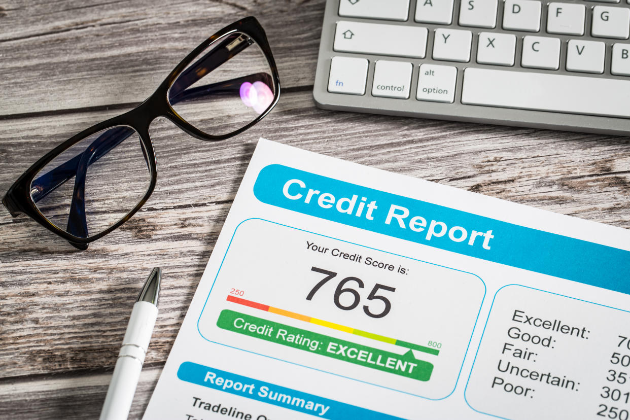 Credit score report against a wooden background alongside a pen, pair of glasses and computer keyboard.