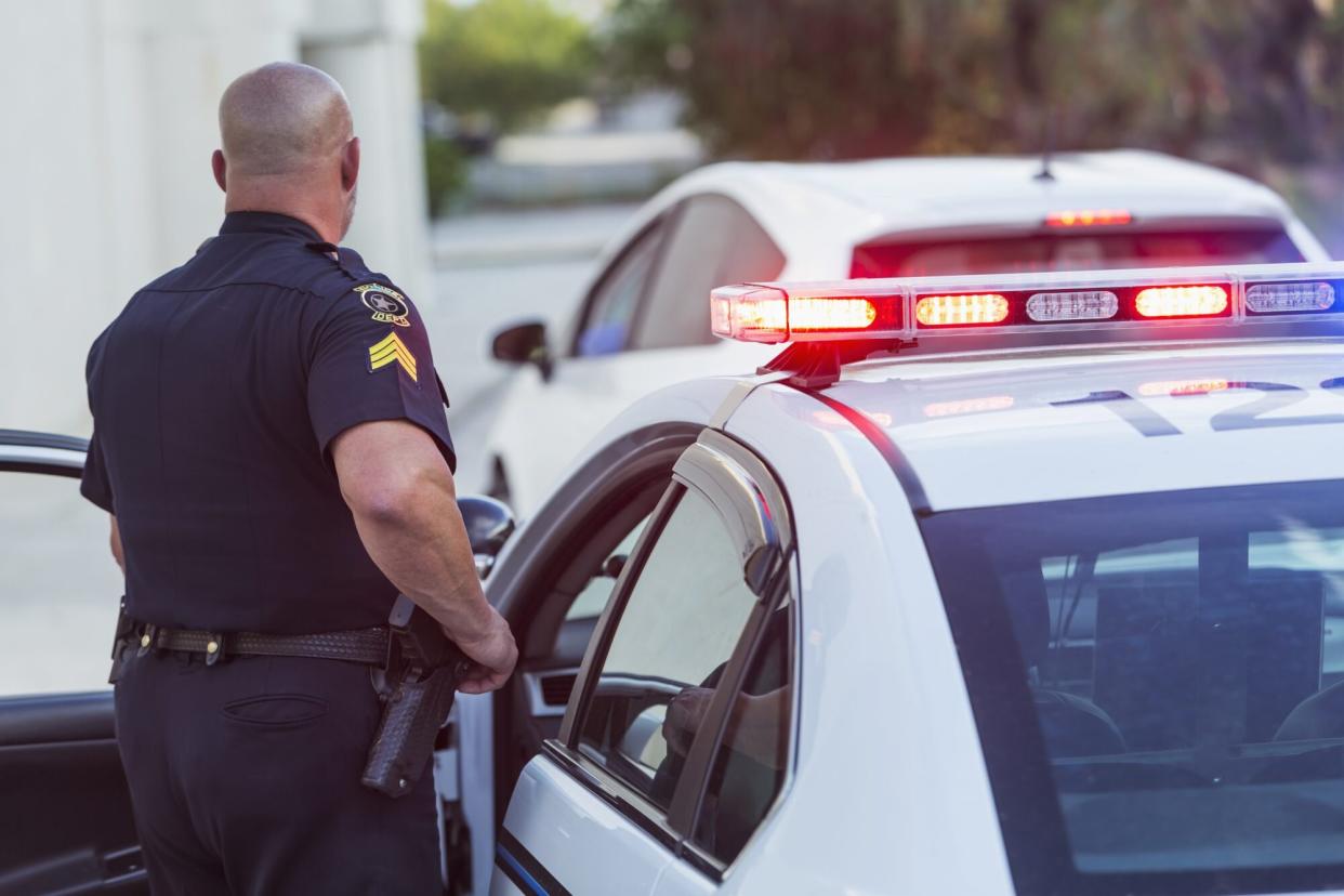 Policeman pulls over a driver for speeding, getting out of police car to write a traffic ticket.