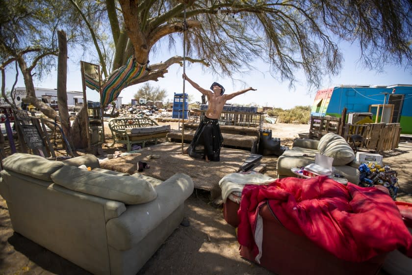 Slab City, CA - April 21: Artist Peter Passalacqua, 51, spins around on a pole on the dance floor at his sprawling slab (named menopause manor by the former owner) consisting of RVs, trailers and junk he collects to turn into artwork. "I came out here to get famous as an artist-that's my ticket out of here," Passalacqua said. Slab City, an unincorporated, off-the-grid squatter community who like to live outside of mainstream society, consisting before the pandemic, of partially snowbirds, artists and freedom-seeking people in the Sonoran Desert, Imperial County, and on the East side the Salton Sea. The Slabs, as the community is known, gets its name from concrete slabs that remained after the World War II Marine Corps Camp Dunlap training camp that was torn down. The remote enclave is known for attracting people who want to live outside mainstream society and has no connection to the main power grid, a general lack of basic amenities, no trash or water services, Streets consist of hardened dirt and most structures are built from salvaged materials. Dogs roam the community that was created by transient, freedom-seeking people, all living off the grid in RVs, broken-down school buses. trailers and tents. Photo taken on Wednesday, April 21, 2021 in Slab City, CA. (Allen J. Schaben / Los Angeles Times)